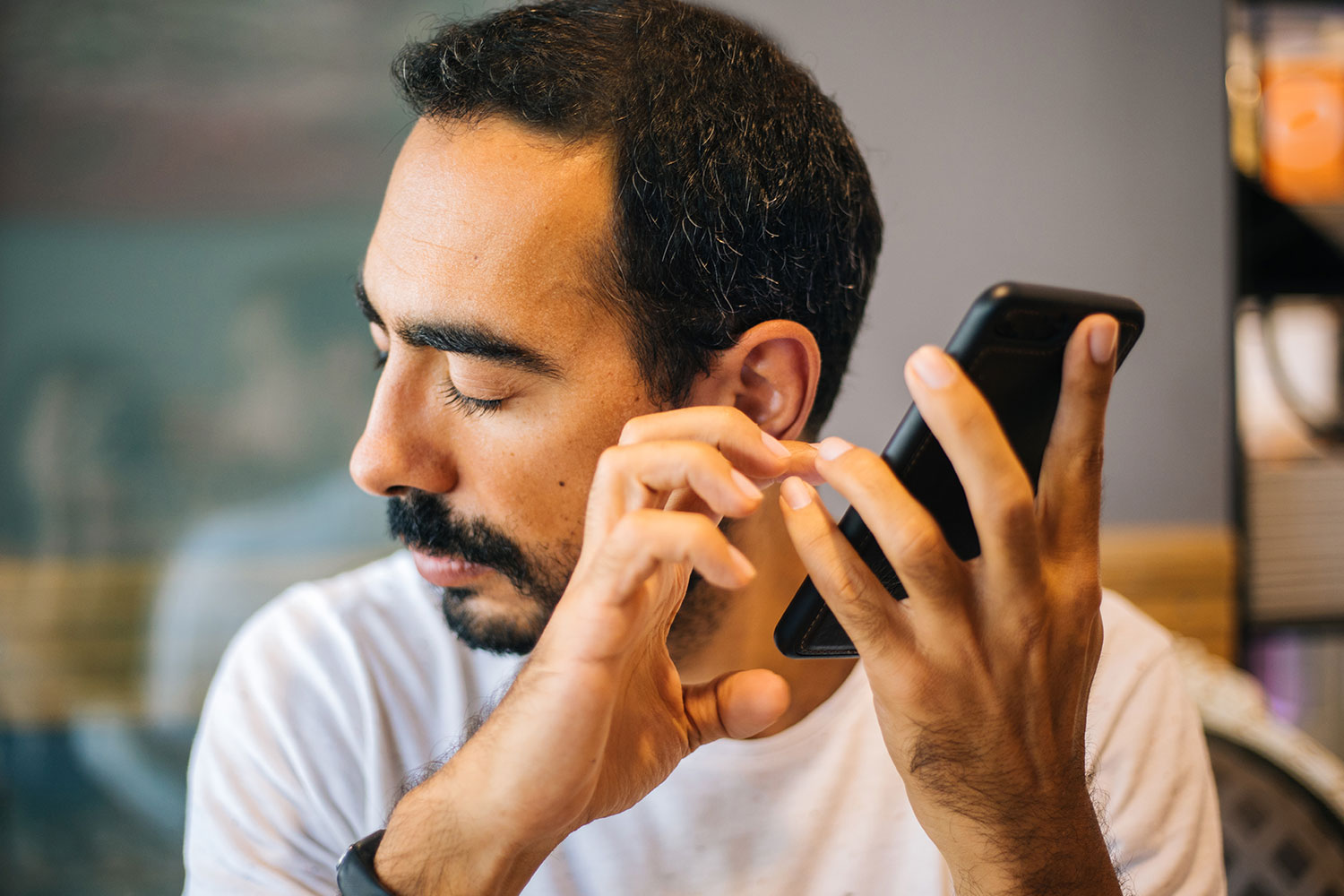 Visually impaired man using a smartphone with the screen turned off, relying on touch and audio cues, in a dimly lit environment.