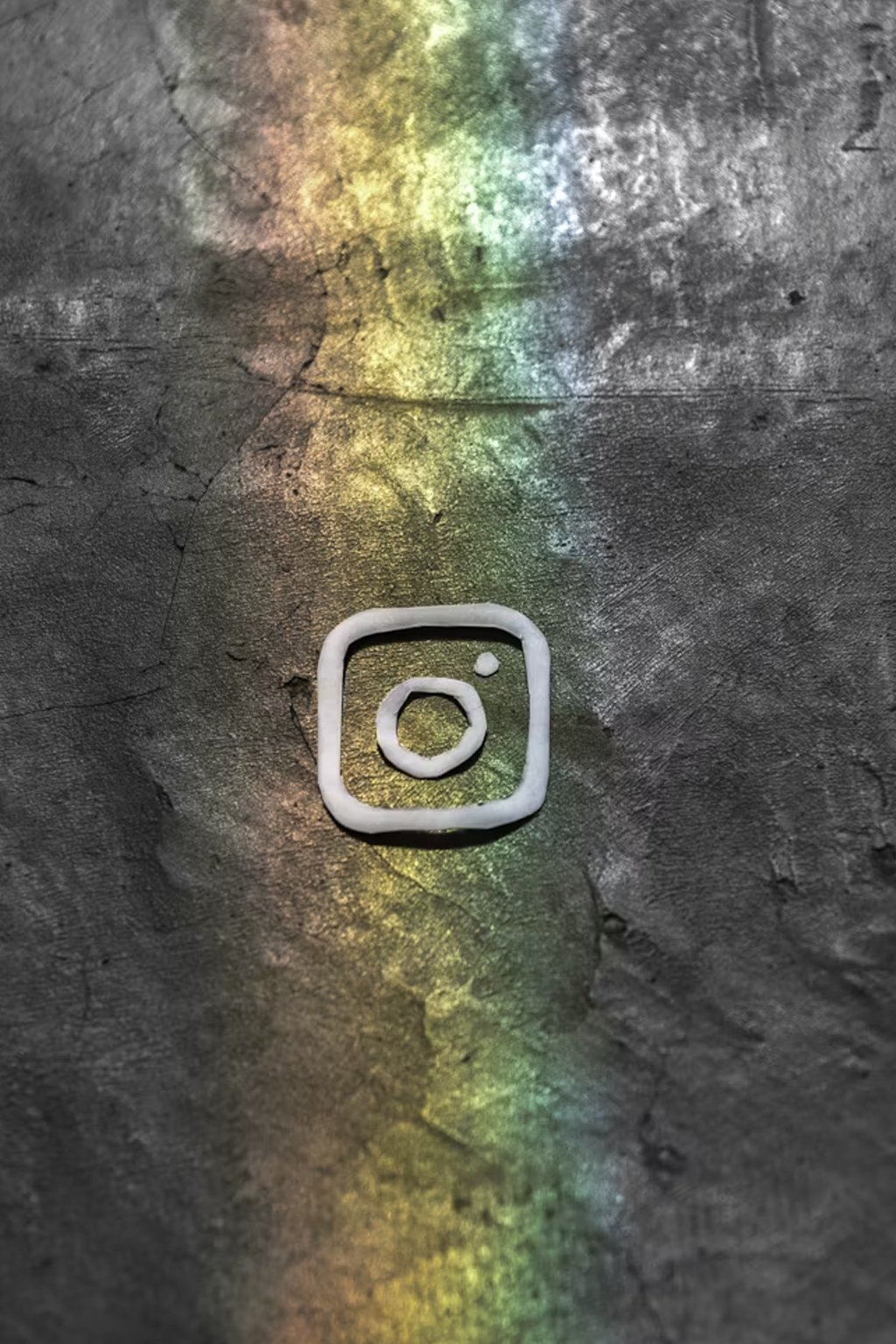 Creative representation of Instagram logo made from plaster on a textured wall with colored light effects.