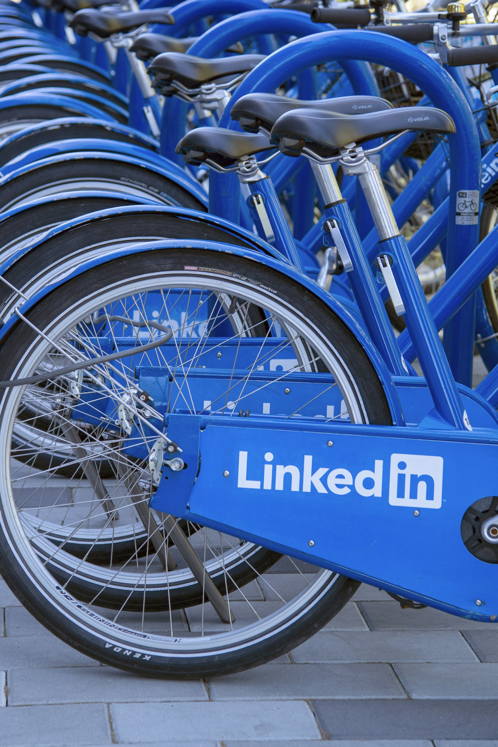 Row of blue bicycles for rent with LinkedIn branding on the frame, lined up in a city bike sharing station.
