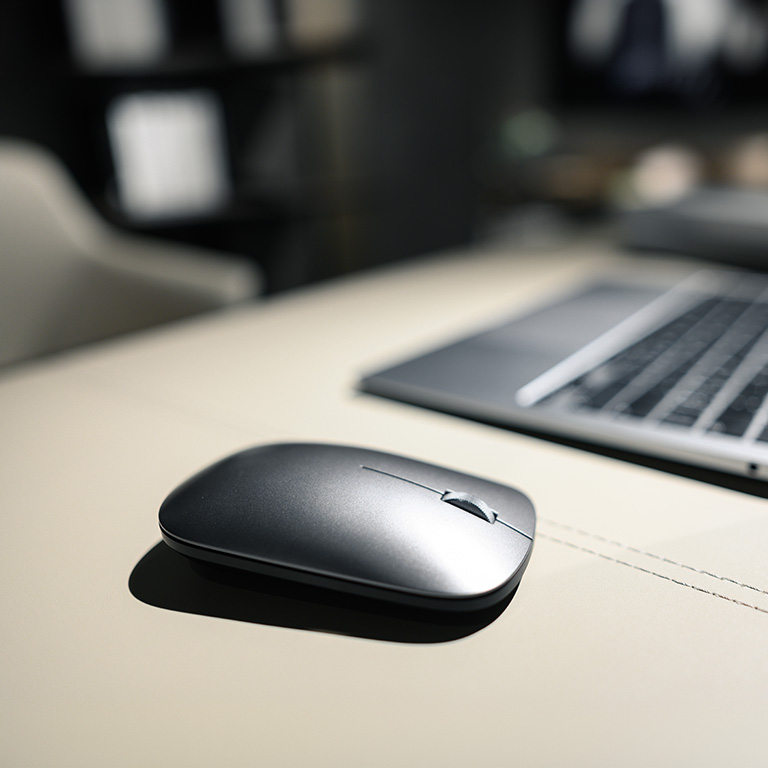 Sleek wireless mouse on a light table surface in a modern office setup with soft lighting, next to a blurred laptop in the background.